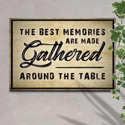 Close view of the tan Gathered Around the Table canvas sign on a gray wall beside green leaves