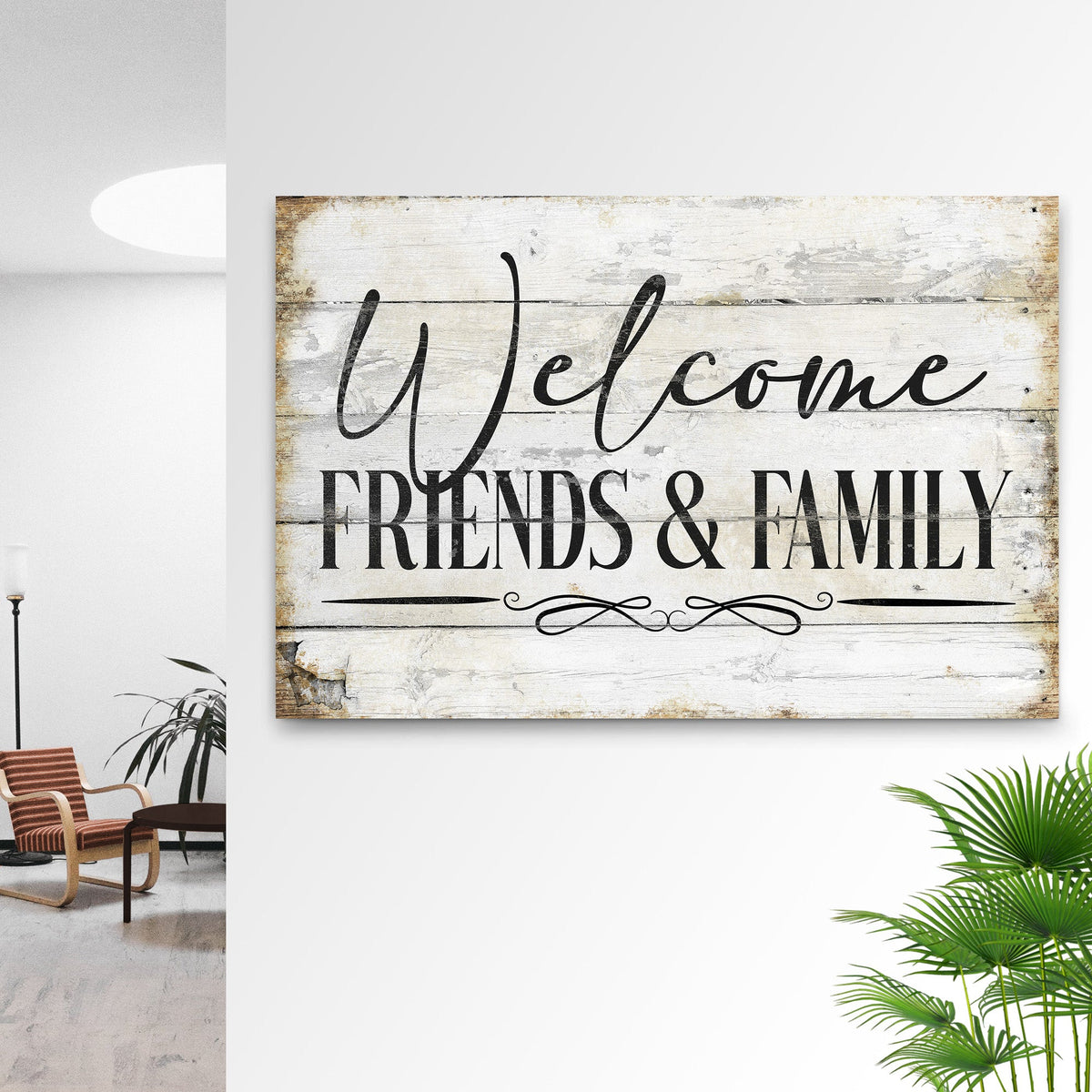 White Welcome Friends and Family canvas sign on a white wall beside palm leaves and an armchair