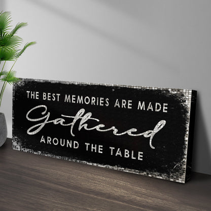Black Gathered Around the Table canvas sign leaning against a gray wall on a wood floor