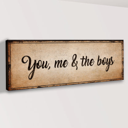 Angled view of the tan You, me & the boys canvas sign on a white wall, showing its dark distressed border