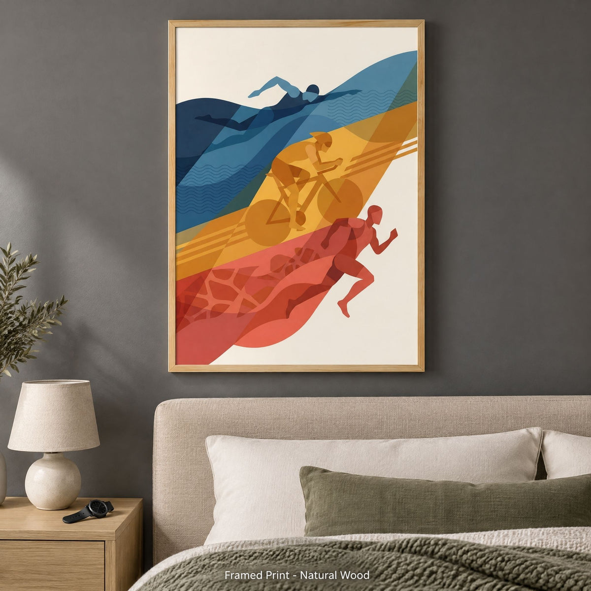 The same triathlon print in a light natural wood frame, above a bed on a charcoal wall