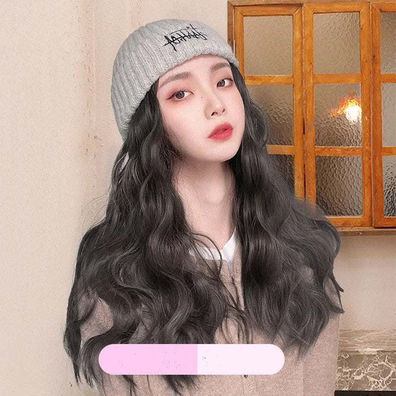 Woman wearing grey embroidered knit beanie hat with attached long wavy dark brown wig hair extensions