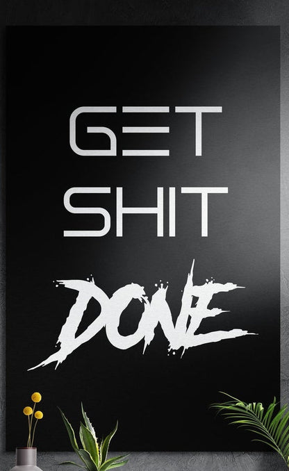 Black brush script Get Sh*t Done brushed aluminum wall art on a dark textured wall above potted plants