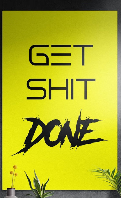 Yellow brush script Get Sh*t Done brushed aluminum wall art on a dark textured wall above potted plants