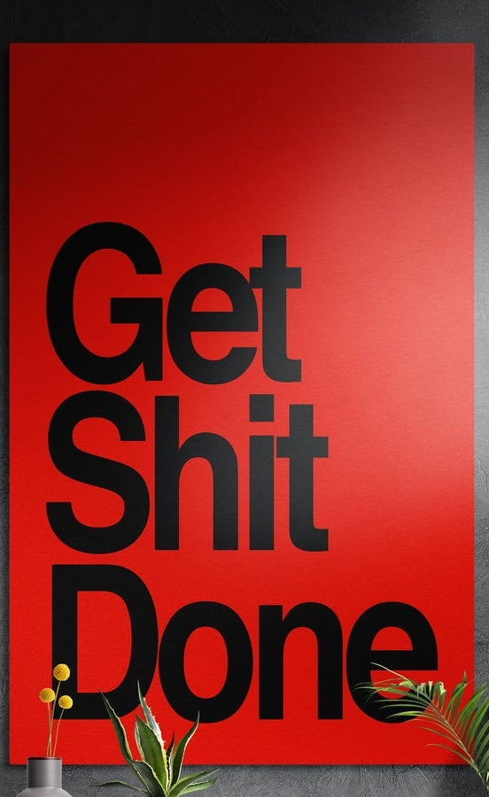 Black on red bold Get Sh*t Done brushed aluminum wall art on a dark textured wall above potted plants