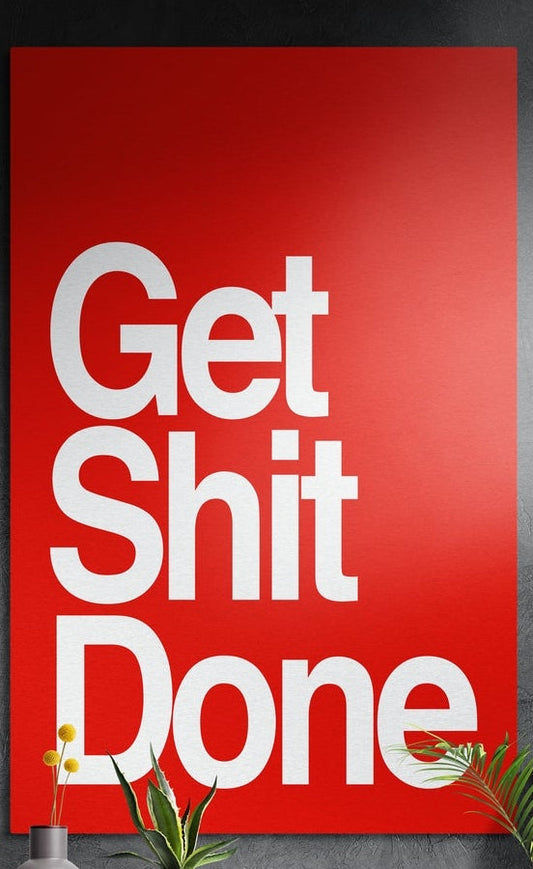 White on red bold Get Sh*t Done brushed aluminum wall art on a dark textured wall above potted plants
