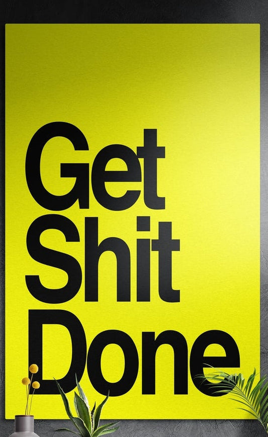 Black on yellow bold Get Sh*t Done brushed aluminum wall art on a dark textured wall above potted plants