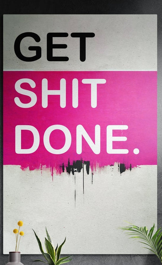 Pink band drip Get Sh*t Done brushed aluminum wall art on a dark textured wall above potted plants