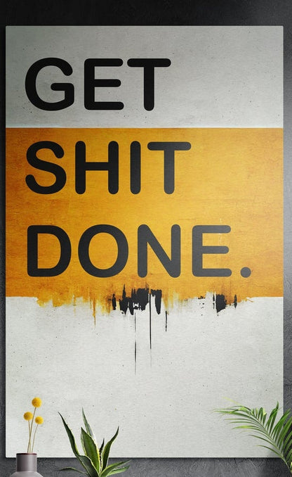 Orange band drip Get Sh*t Done brushed aluminum wall art on a dark textured wall above potted plants