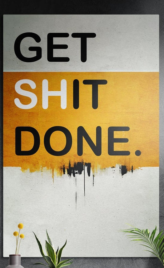 Amber drip two-tone Get Sh*t Done brushed aluminum wall art on a dark textured wall above potted plants
