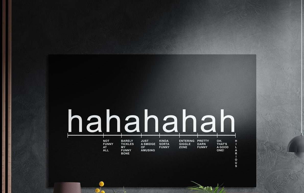 Laughter scale typography on black brushed aluminum wall art on a dark wall above a vase and plants