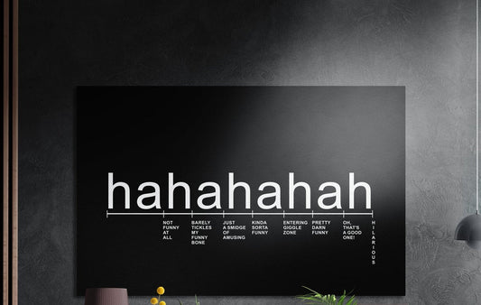 Laughter scale typography on black brushed aluminum wall art on a dark wall above a vase and plants