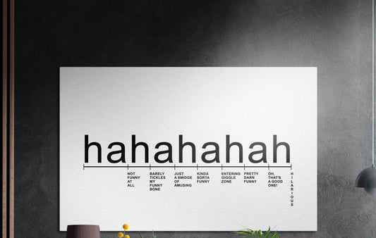 Hahaha laughter scale typography brushed aluminum wall art on a dark textured wall with plants below