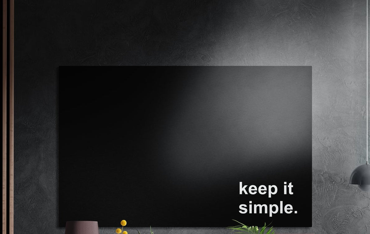 Keep it simple white text on black brushed aluminum wall art on a dark textured wall above potted plants