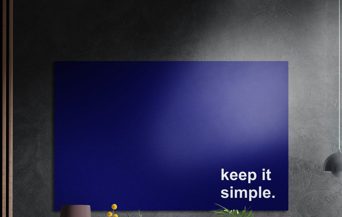 Keep it simple white text on navy brushed aluminum wall art on a dark textured wall above potted plants