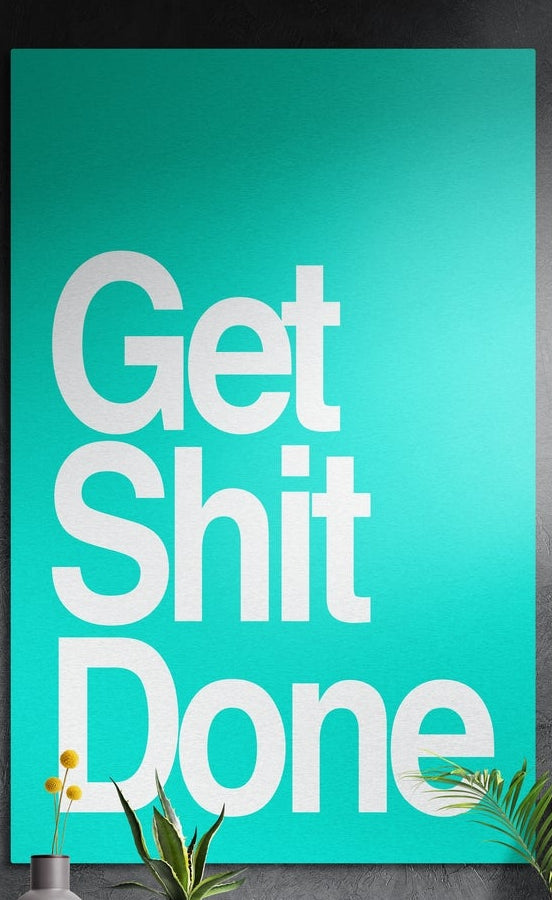 Teal bold Get Sh*t Done brushed aluminum wall art on a dark textured wall above potted plants
