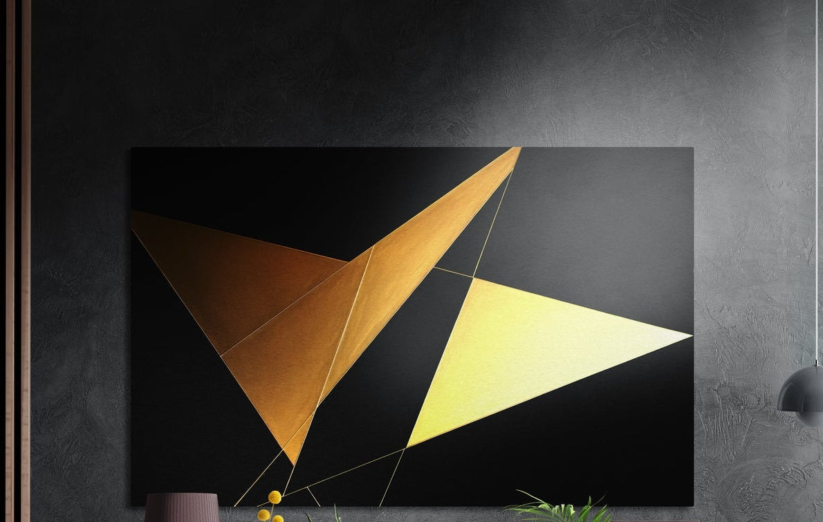 Gold triangles on black brushed aluminum wall art on a dark textured wall above a vase and plants