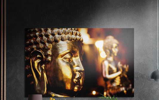Golden Buddha face close up brushed aluminum wall art on a dark gray wall above a mauve lamp and plants