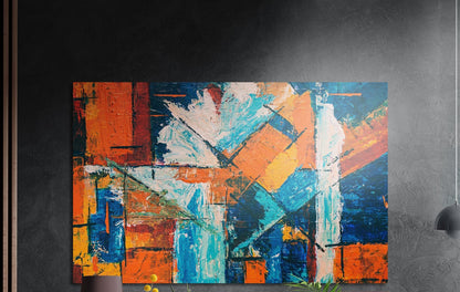 Orange and blue color block abstract brushed aluminum wall art on a dark wall above the tips of potted plants