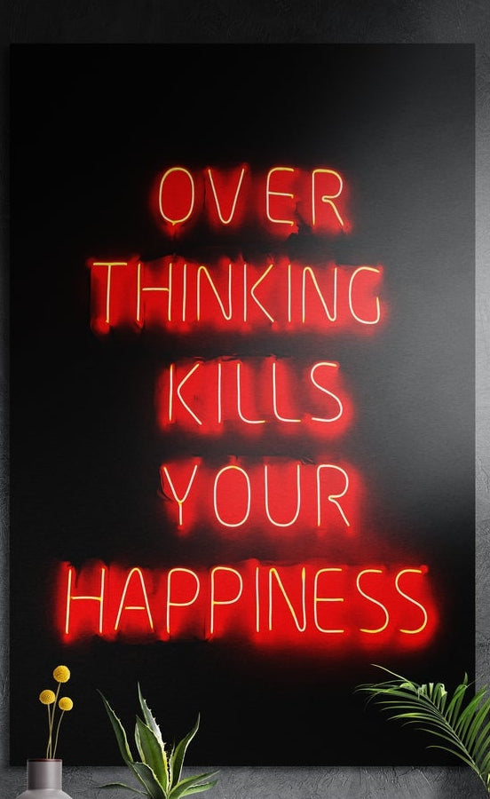 Red neon overthinking quote brushed aluminum wall art on a dark textured wall above a vase of yellow flowers and plants