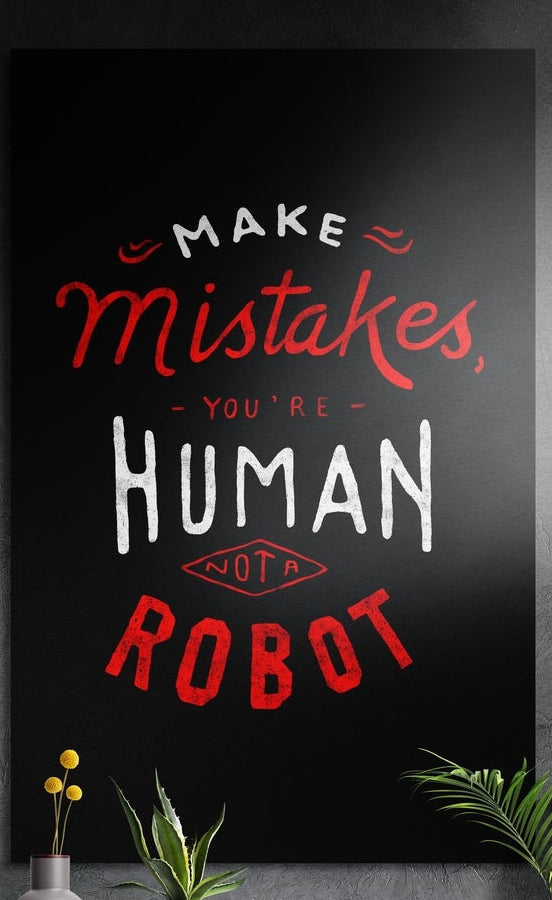 Make mistakes you are human lettering brushed aluminum wall art on a dark textured wall above potted plants
