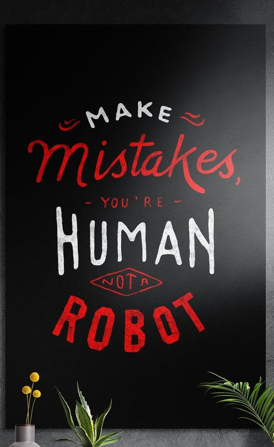 Make mistakes you are human lettering brushed aluminum wall art on a dark textured wall above potted plants