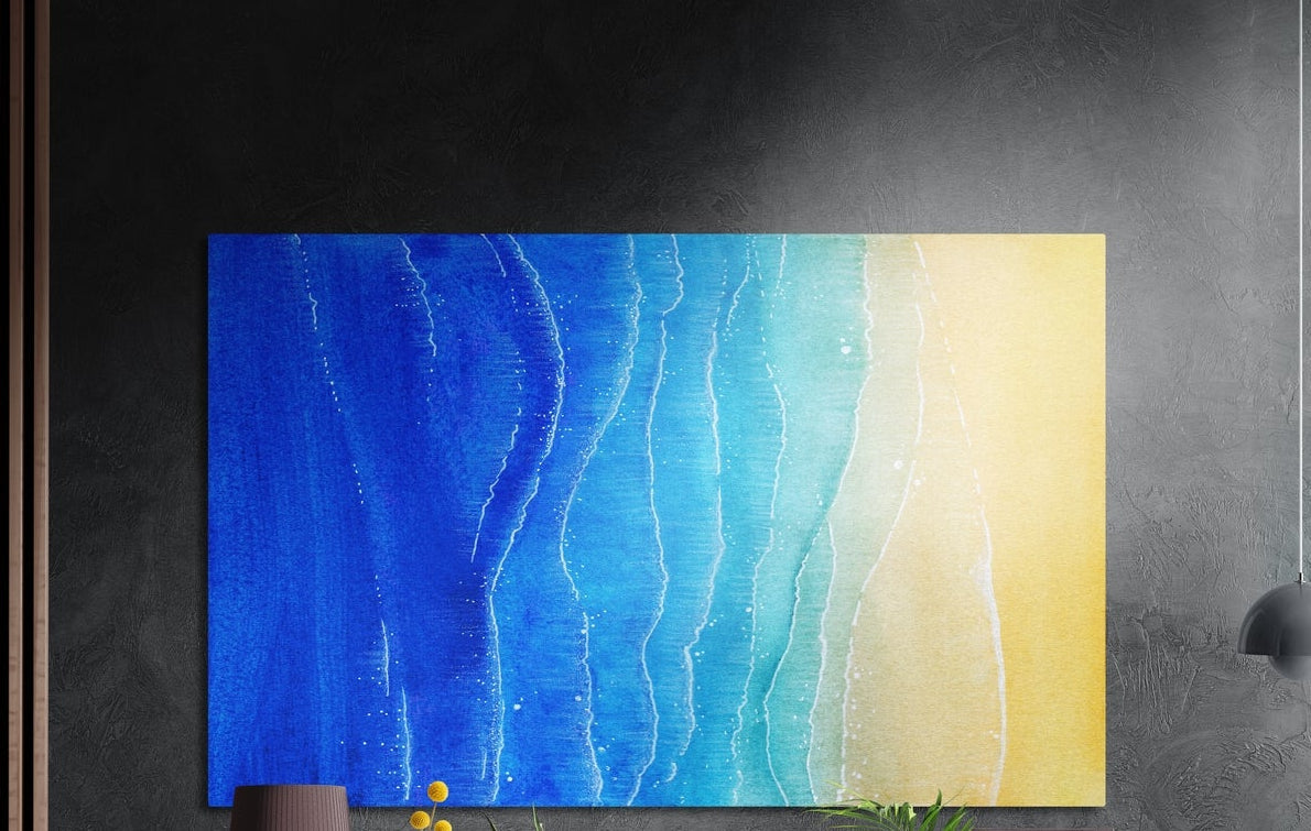 Blue ocean shoreline abstract brushed aluminum wall art on a dark textured wall, a lamp and plant tops below