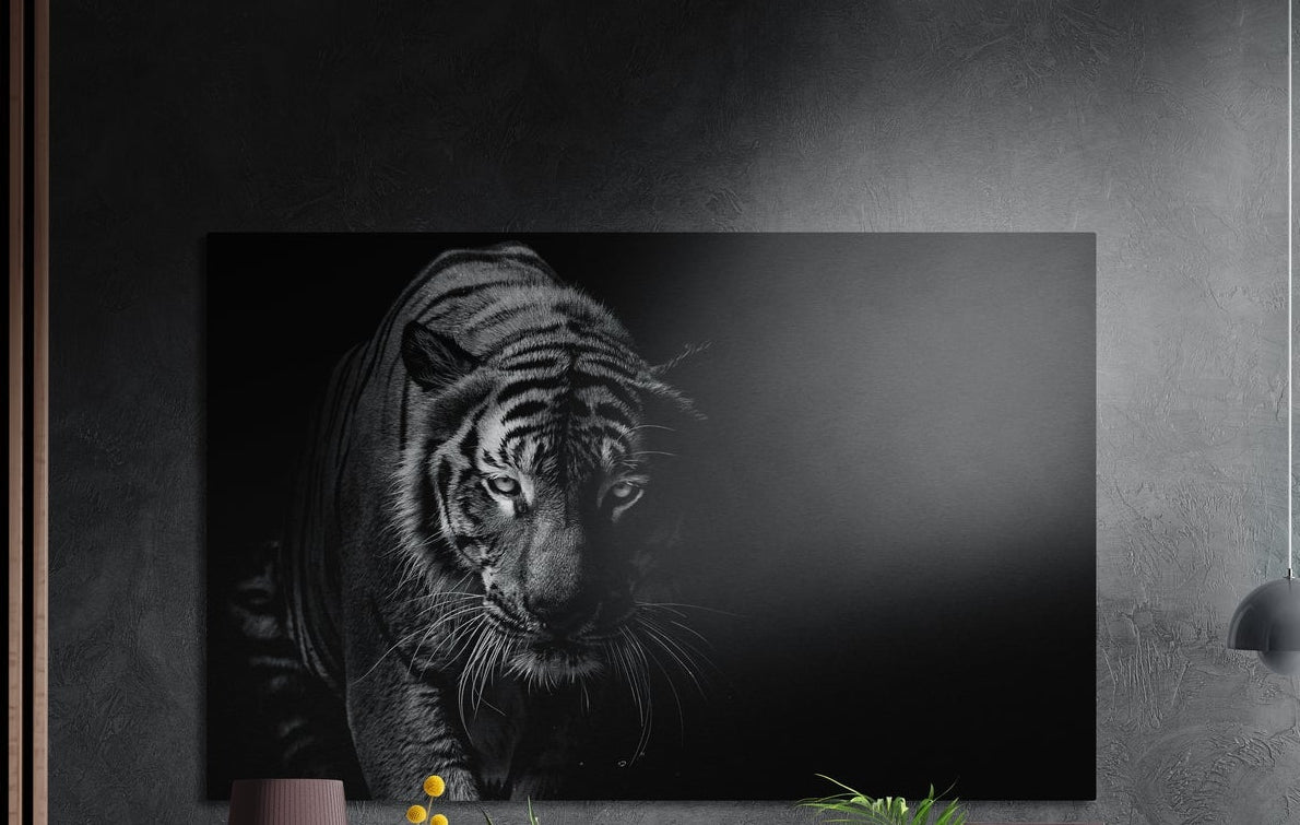 Black and white prowling tiger brushed aluminum wall art on a dark wall above a sideboard with yellow flowers