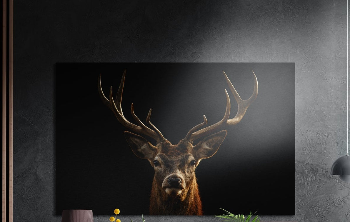 Antlered stag portrait brushed aluminum wall art on a dark wall above a sideboard with yellow flowers