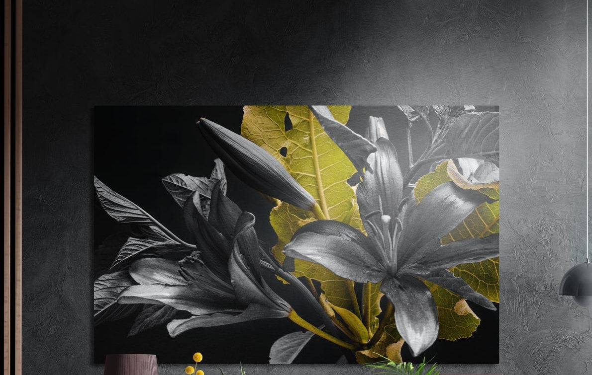 Monochrome lilies with golden leaves brushed aluminum wall art on a dark textured wall beside wood slats and a lamp