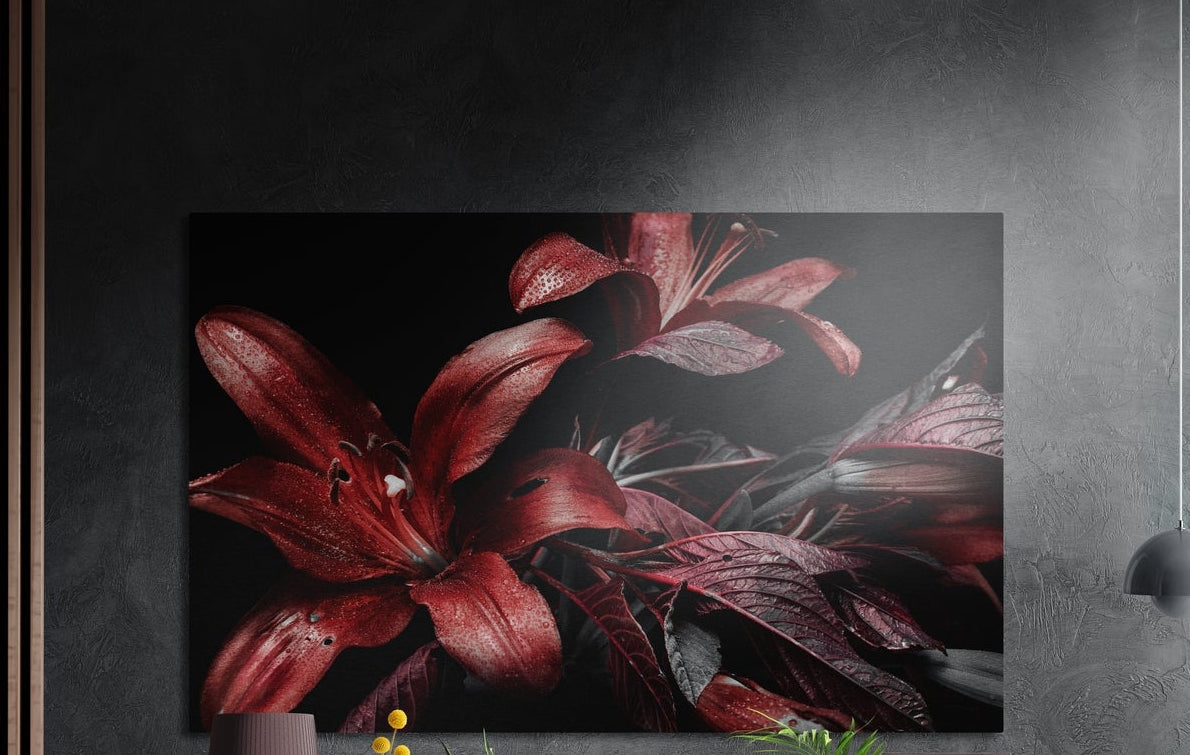 Red lilies on black brushed aluminum wall art on a dark textured wall above a vase and plants