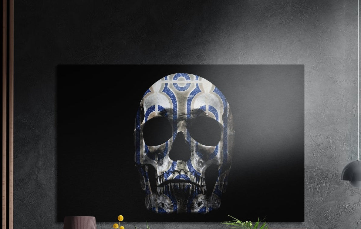 Blue and white pattern skull on black brushed aluminum wall art on a dark textured wall above potted plant tops