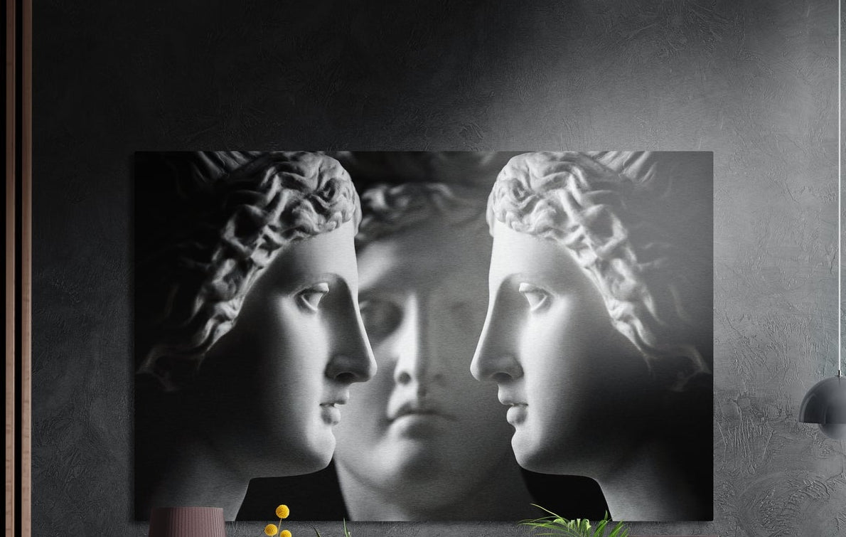 Three classical marble busts in profile brushed aluminum wall art on a dark wall above the tips of potted plants