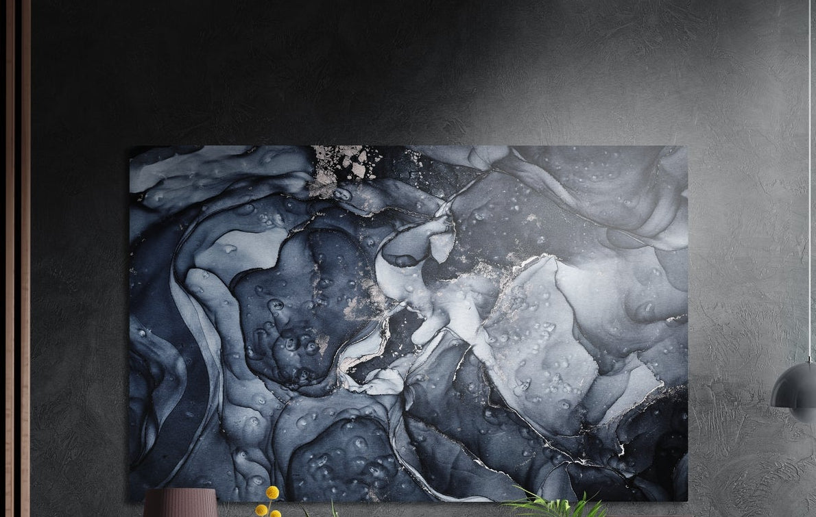 Charcoal and navy ink marble brushed aluminum wall art on a dark wall above the tips of potted plants