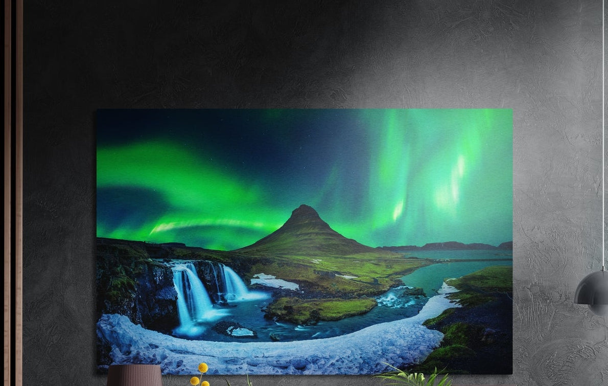 Northern lights over mountain waterfalls brushed aluminum wall art on a dark textured wall with plants below