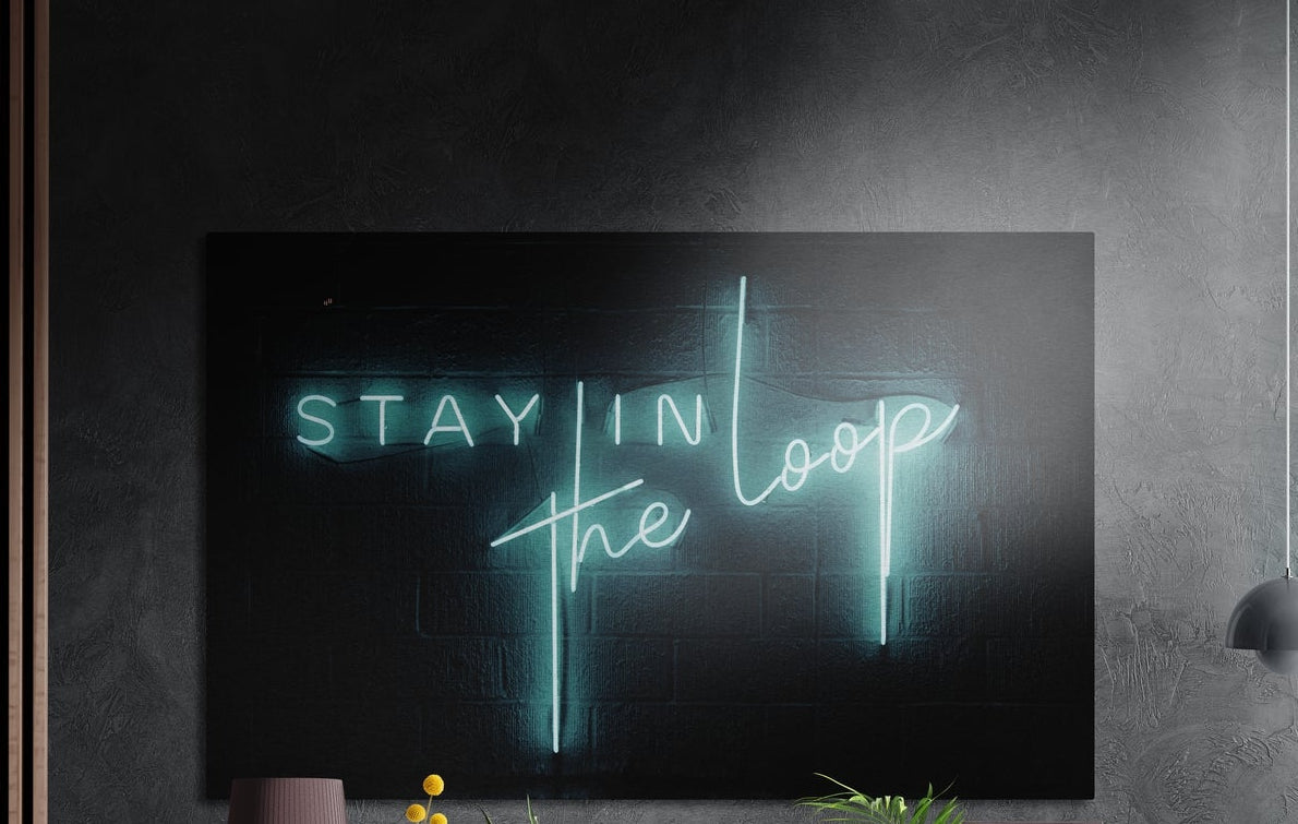 Teal neon lettering reading Stay in the Loop on dark brick, brushed aluminum wall art on a dark textured wall