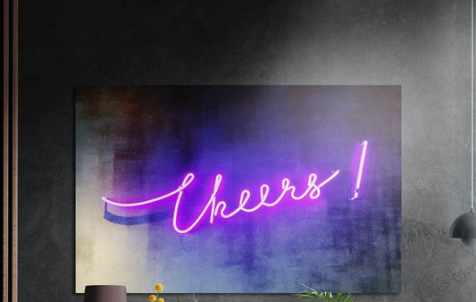 Pink neon Cheers sign brushed aluminum wall art on a dark textured wall above a vase and plants