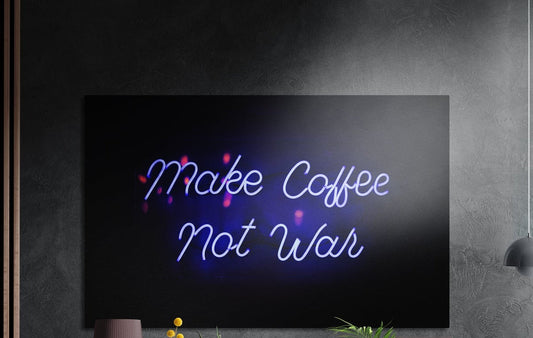 Make Coffee Not War blue neon script brushed aluminum wall art on a dark gray wall above yellow flowers