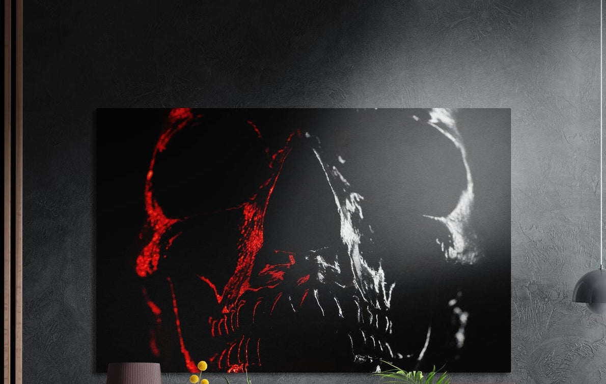 Split red and white skull on black brushed aluminum wall art on a gray concrete wall with a lamp and plants below