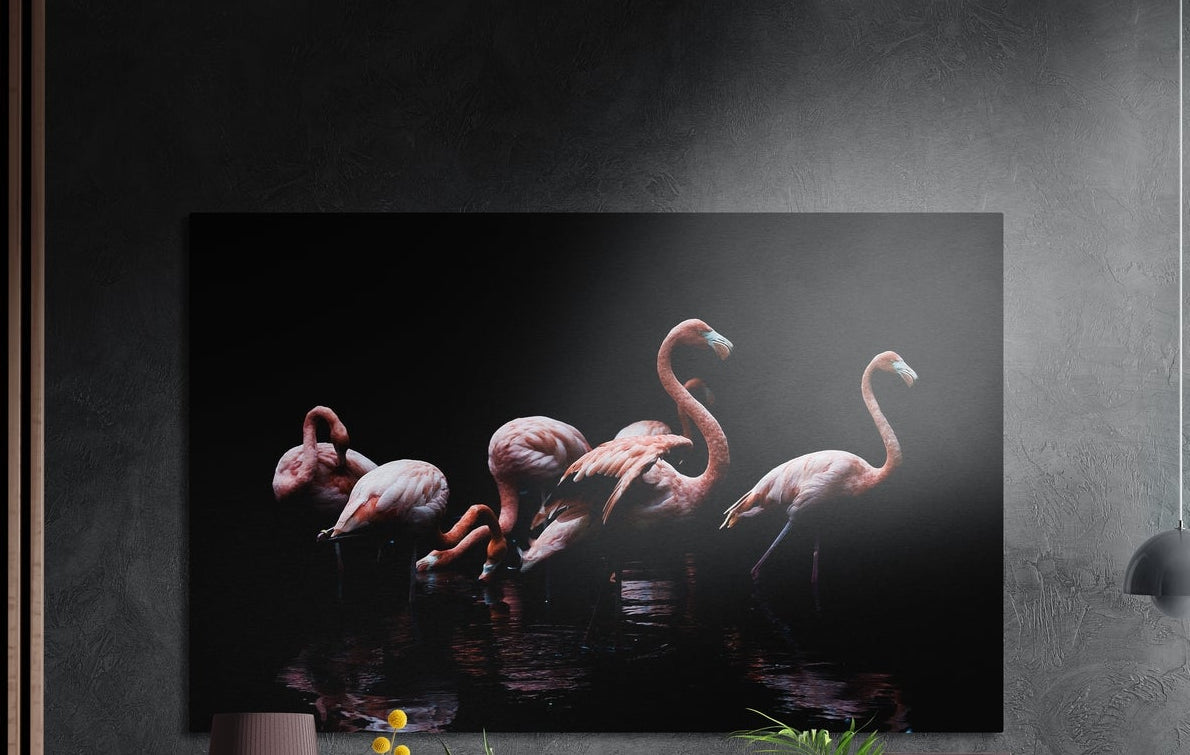 Pink flamingo flock on black brushed aluminum wall art on a dark wall above a sideboard with yellow flowers