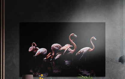 Pink flamingo flock on black brushed aluminum wall art on a dark wall above a sideboard with yellow flowers