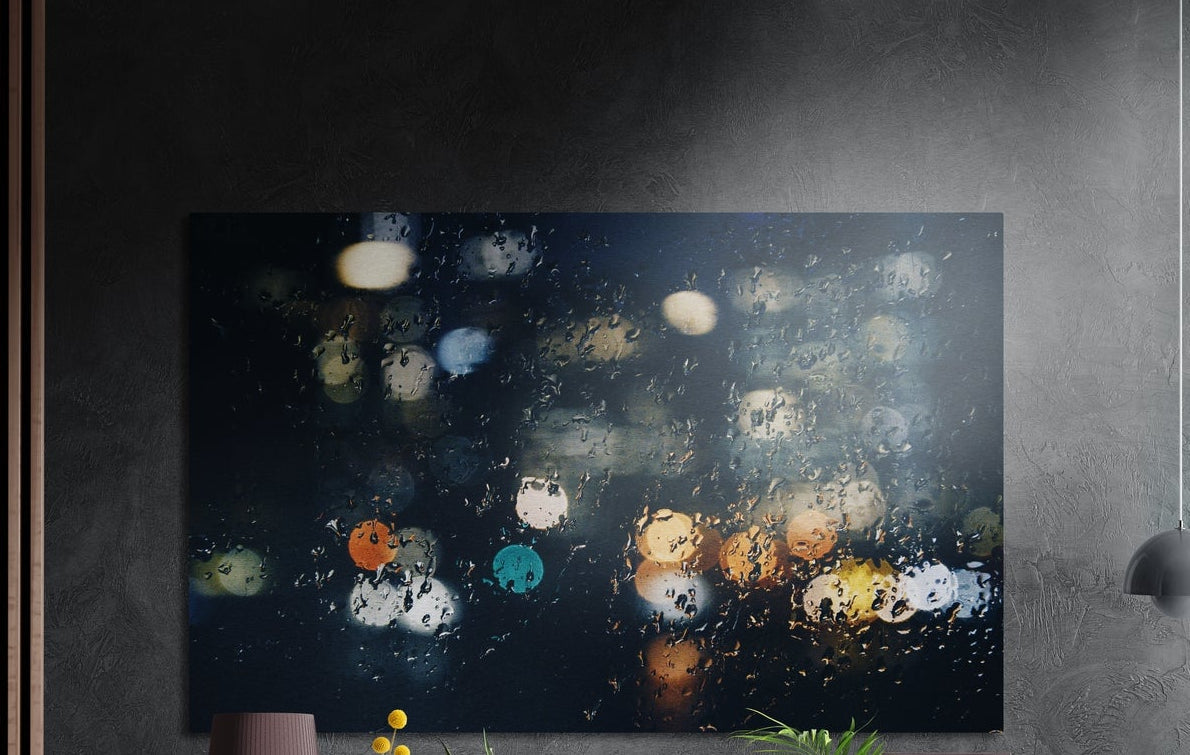 Blurred city lights through rain brushed aluminum wall art on a dark textured wall beside wood slats and a lamp