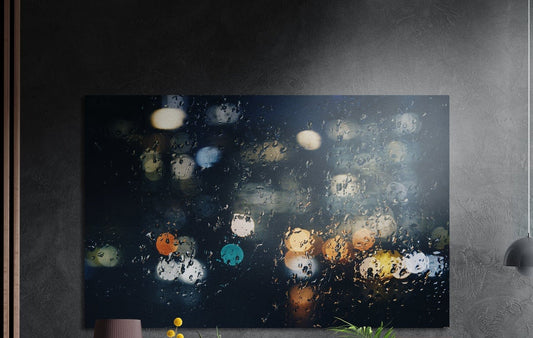 Blurred city lights through rain brushed aluminum wall art on a dark textured wall beside wood slats and a lamp