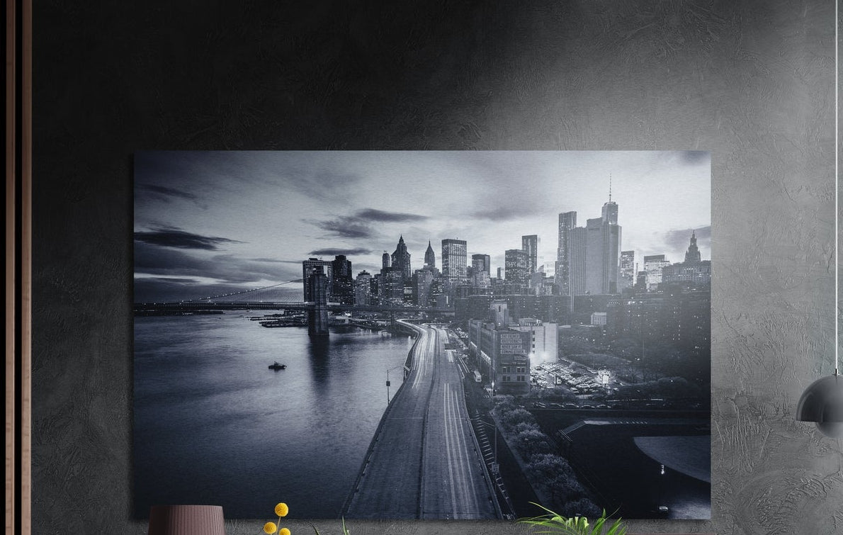 Black and white city skyline by the river brushed aluminum wall art on a dark textured wall beside wood slats and a lamp