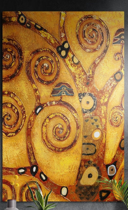 Golden swirl tree of life brushed aluminum wall art on a dark gray wall with plants in front of its lower edge