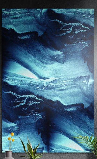 Blue abstract ink wash brushed aluminum wall art on a dark wall behind a vase of yellow flowers and plants