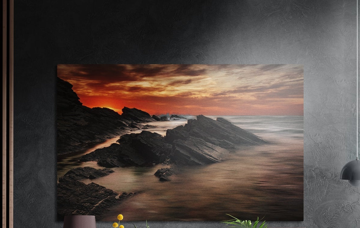 Rocky shore sunset brushed aluminum wall art on a dark gray wall above a sideboard with a vase and plants