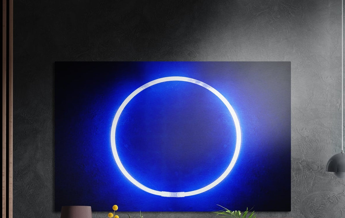 Glowing blue neon ring, brushed aluminum wall art on a dark gray wall above a vase and yellow flowers