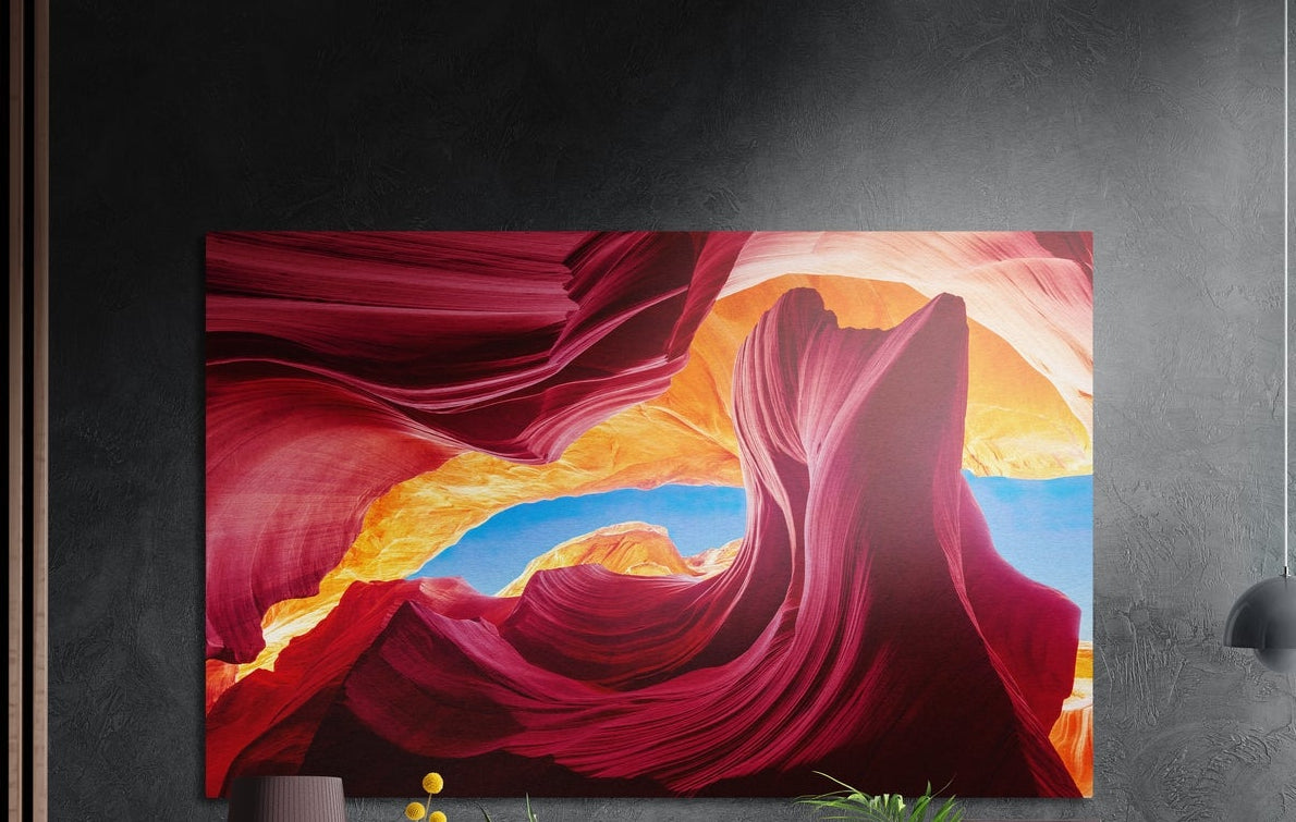Crimson sandstone canyon waves brushed aluminum wall art on a dark textured wall, a lamp and plant tops below