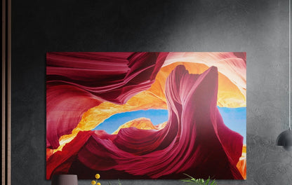 Crimson sandstone canyon waves brushed aluminum wall art on a dark textured wall, a lamp and plant tops below